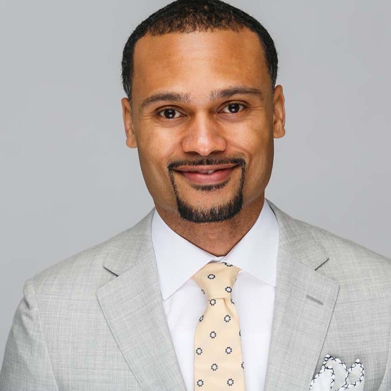 black male light grey suit yellow tie pocket square headshot